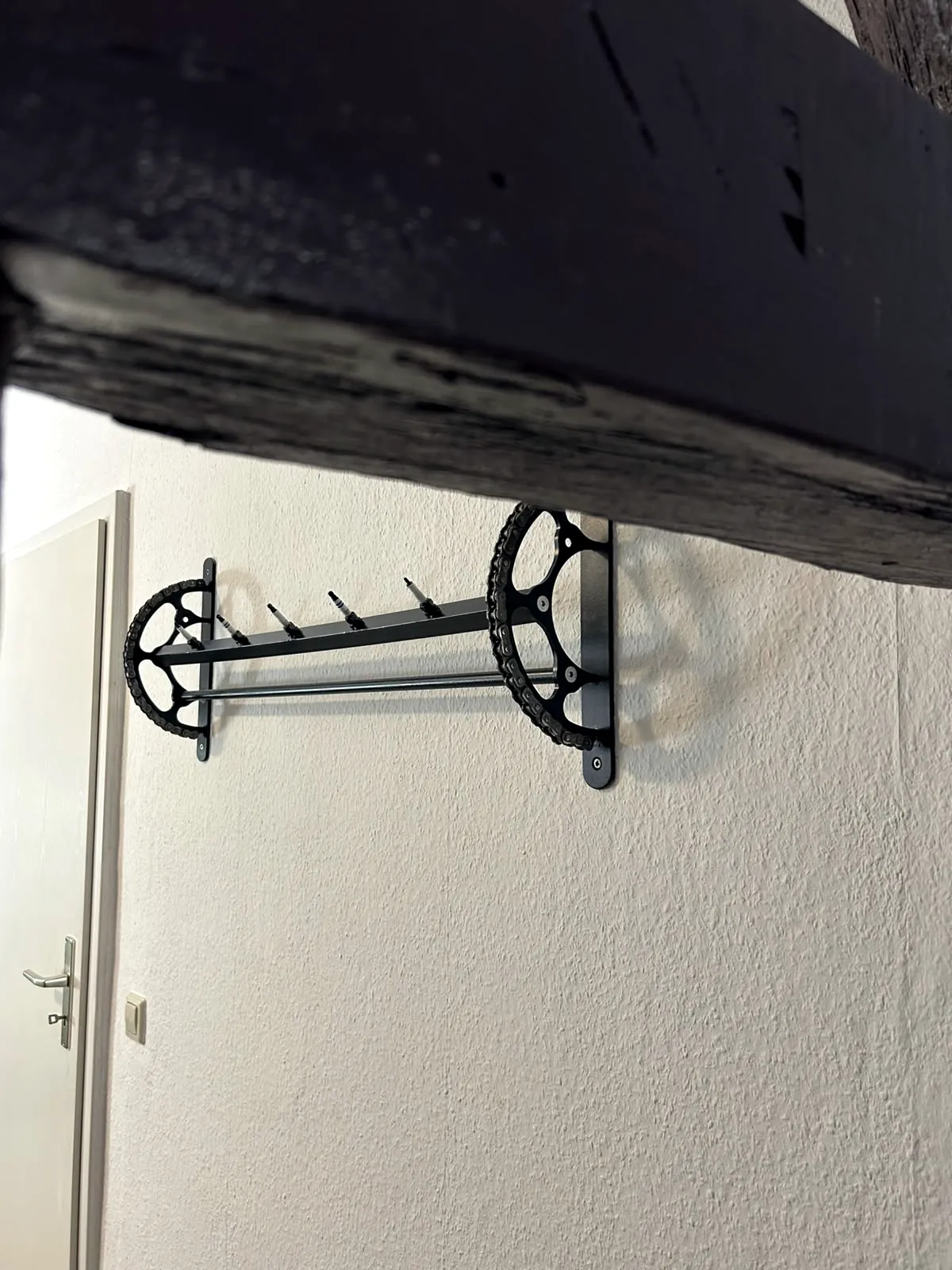 Wandgarderobe aus zwei Kettenblättern mit Kette, Zündkerzen als Haken und Kleiderstange